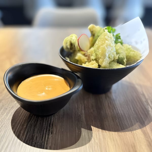 Crispy green tempura with a radish slice and parsley, served with a side of orange dipping sauce.