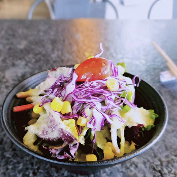 A vibrant side salad with red cabbage, corn, and a cherry tomato in a black bowl.
