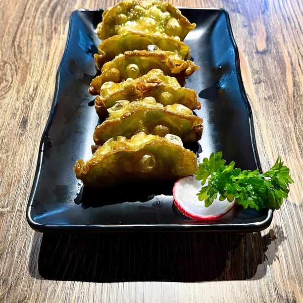 Six golden-fried gyoza dumplings on a black rectangular plate, garnished with parsley and a radish slice.